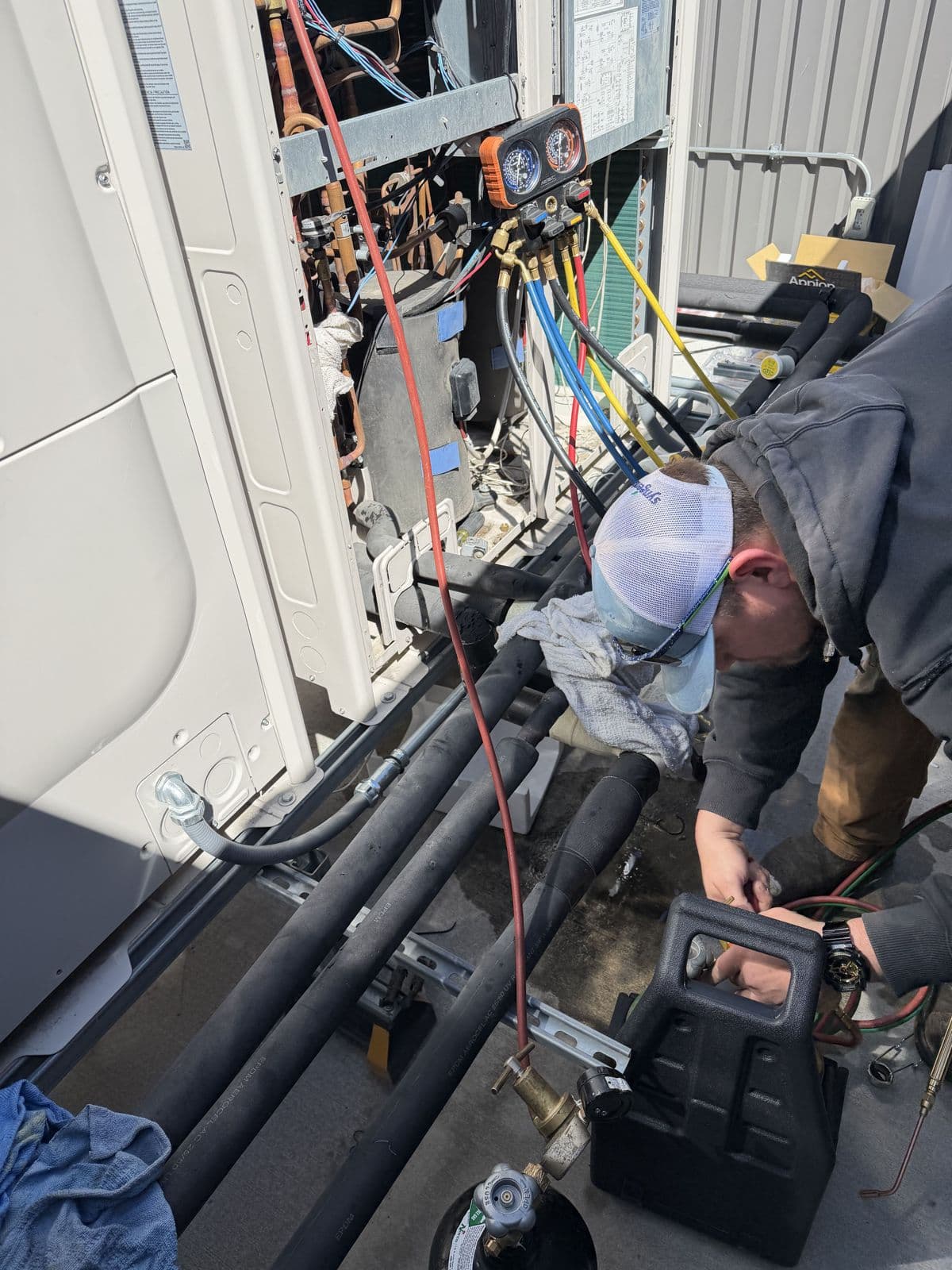 Meridian technician with gauges connected to an outdoor VRF unit, working on its insulated refrigerant lines