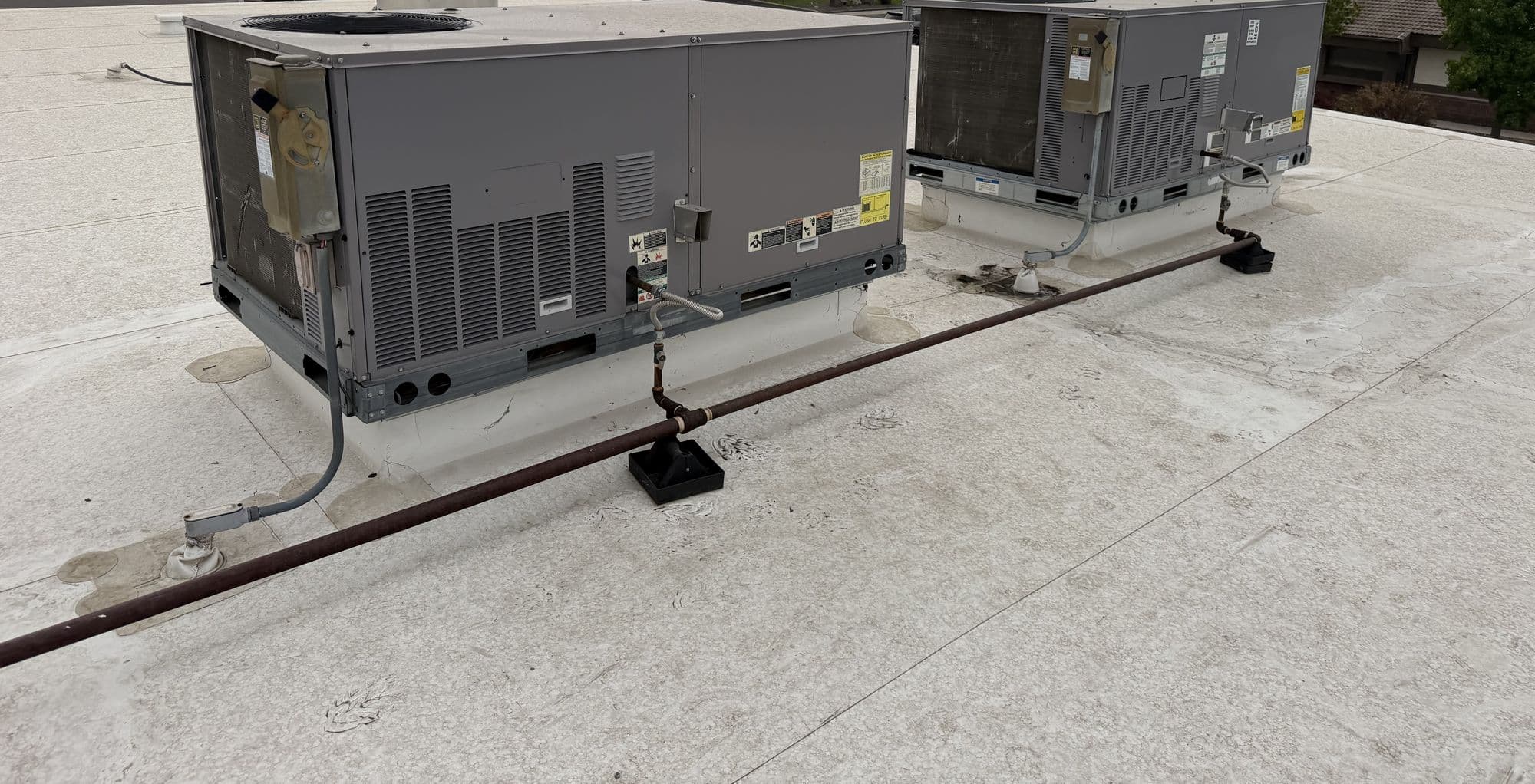 Two packaged rooftop units on a flat commercial roof, with gas piping run on pipe supports