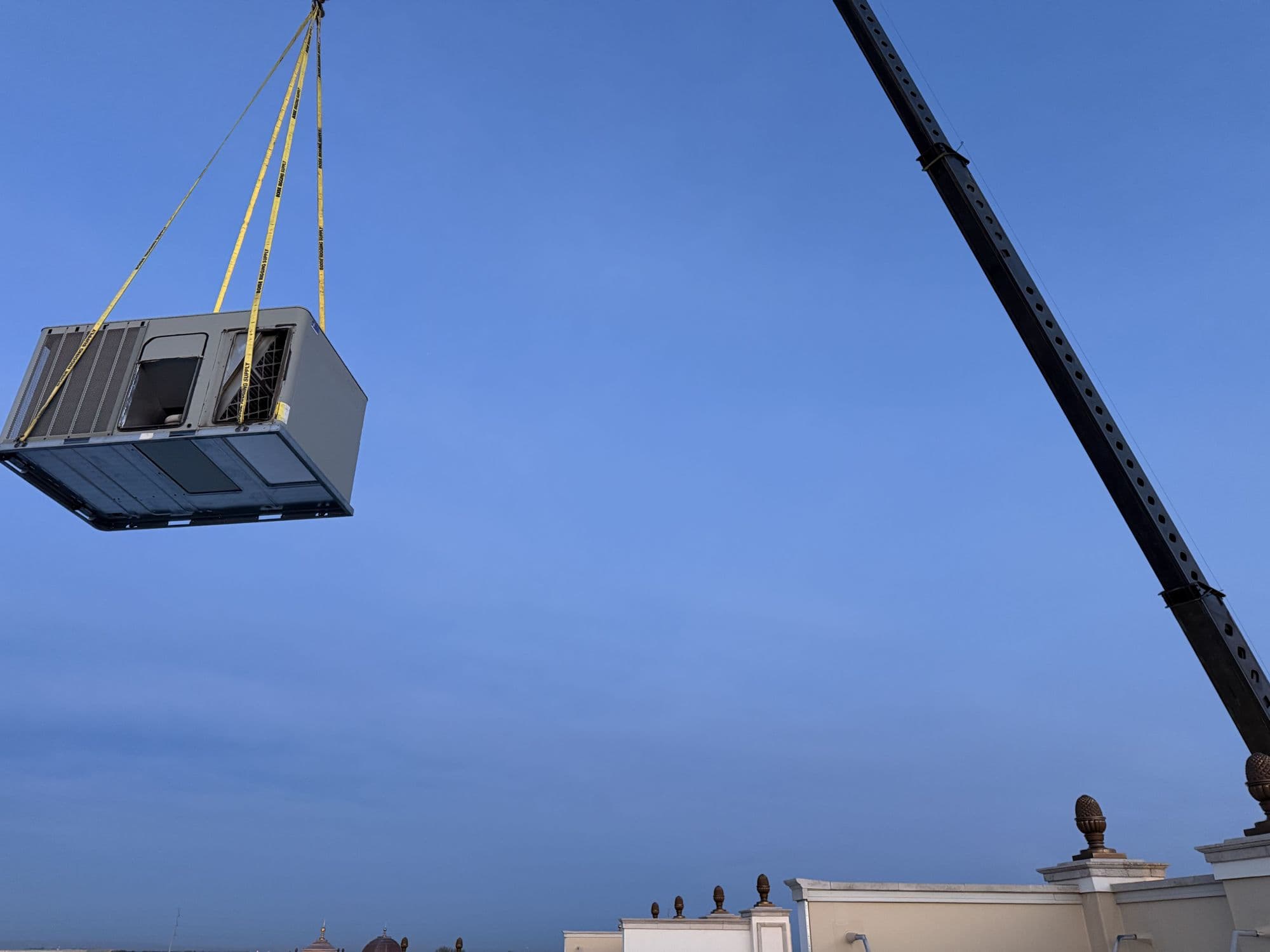 Commercial rooftop unit being lifted by crane onto a building roof