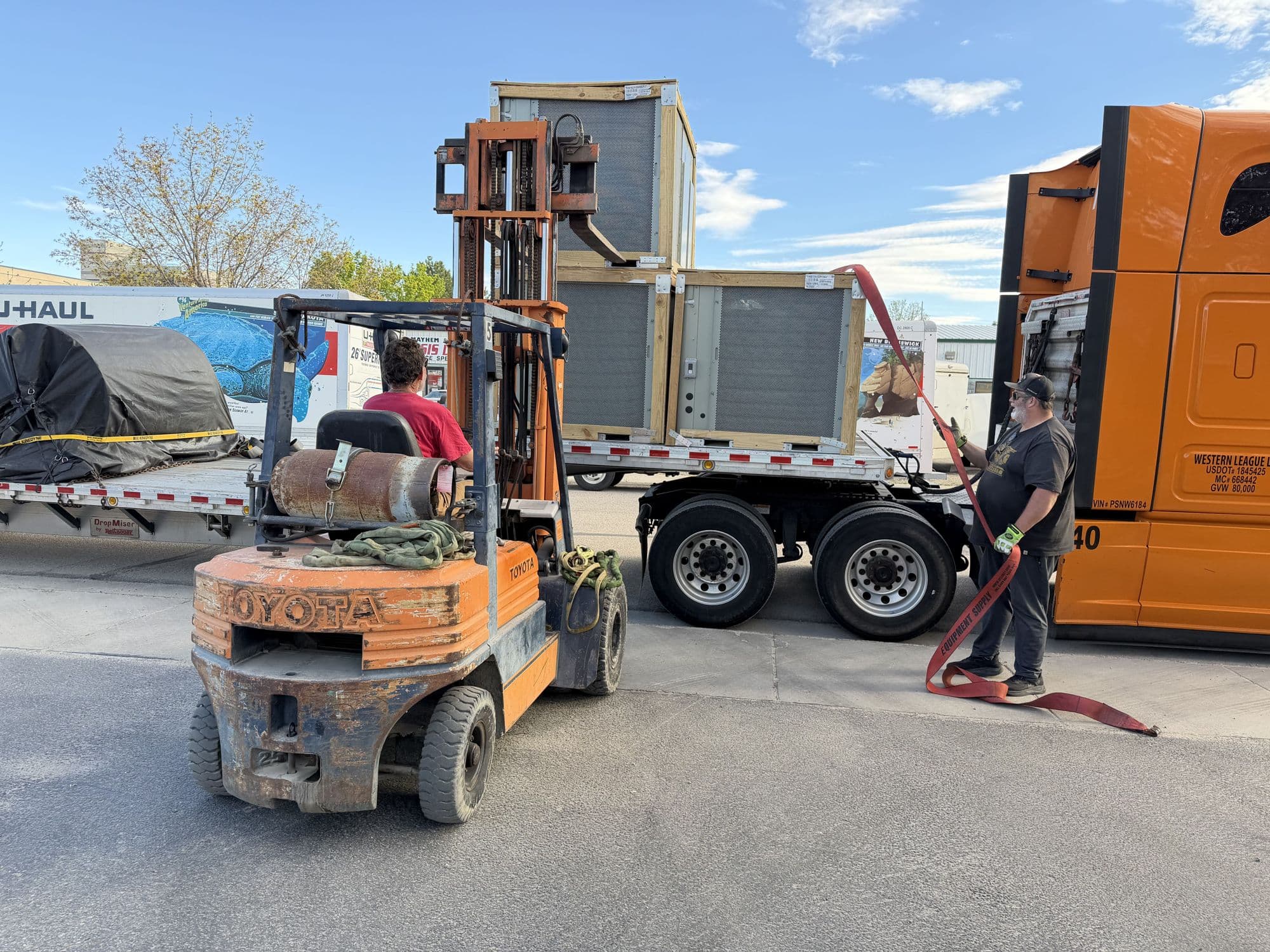 Crated commercial rooftop units being unloaded from a flatbed by forklift for installation